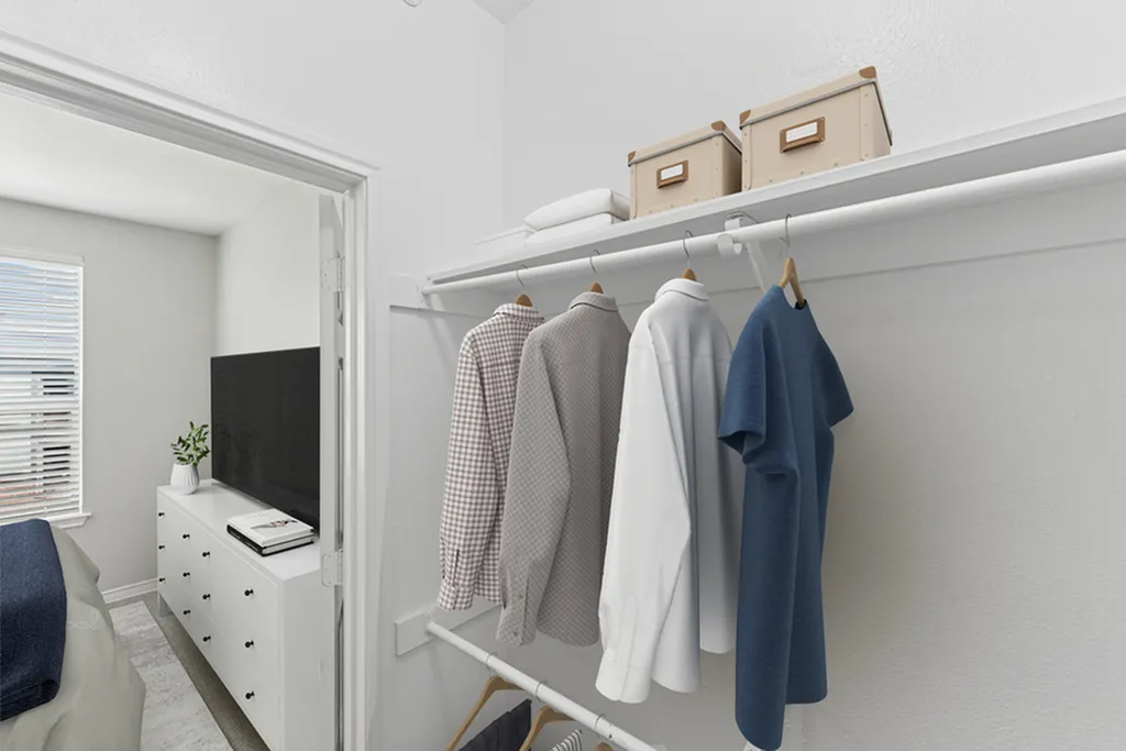 Secondary bedroom closet with dual rods, top shelf with boxes, and shirts on wooden hangers