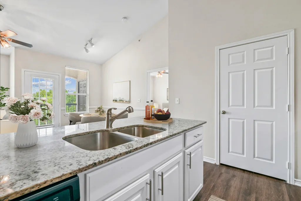 Bright and airy kitchen with elegant granite countertops, fresh flowers, and views of a cozy living area and dining room, offering a warm and inviting atmosphere.