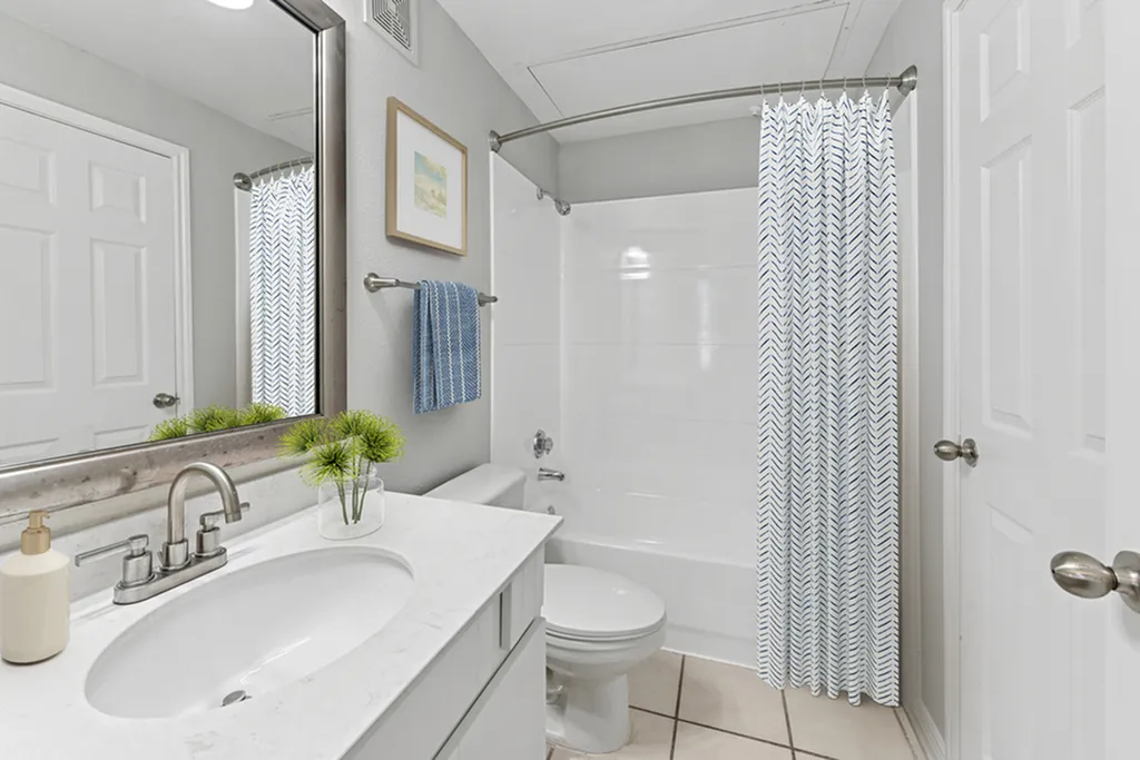 Modern bathroom with sleek fixtures, quartz countertop, large vanity mirror and stylish patterned shower curtain with shower/tub combo.