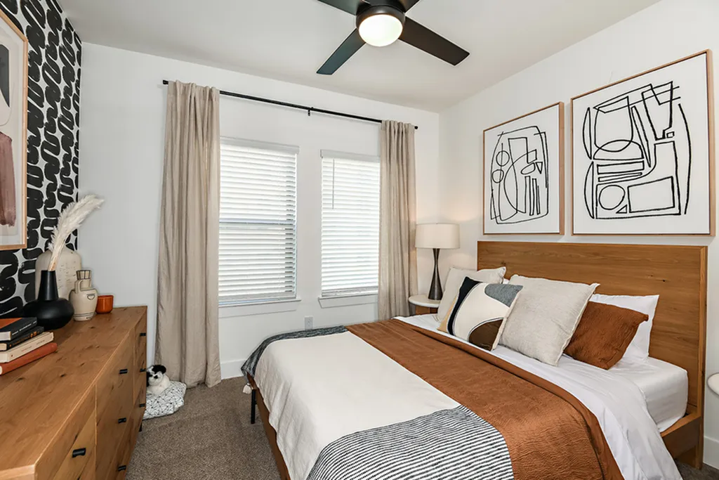 Cozy bedroom with modern decor, featuring a stylish bed with accent pillows, abstract wall art, and a chic wooden dresser.