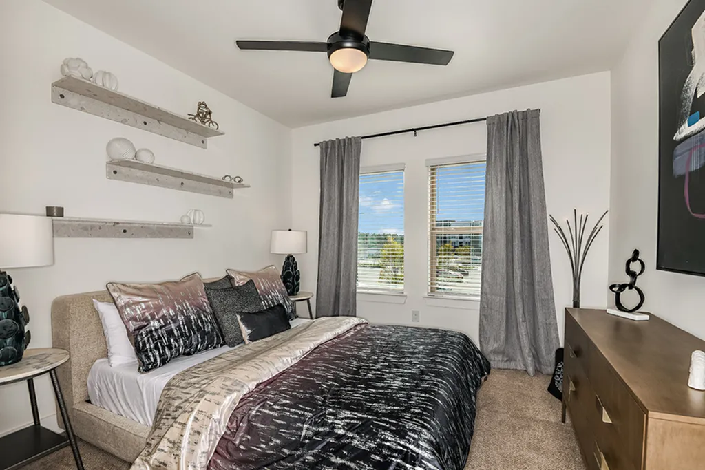 Cozy bedroom with modern decor, featuring stylish bedding, sleek wooden dresser, and large windows welcoming natural light.