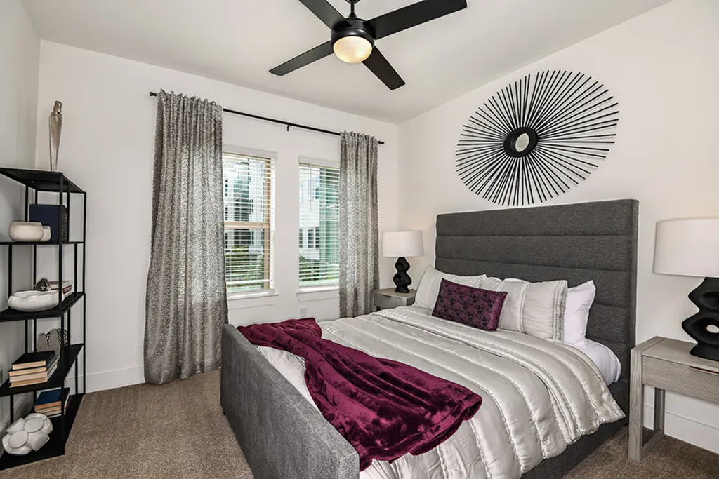 Elegant bedroom with modern decor featuring a plush gray bed, vibrant purple accents, contemporary art piece, and ample natural light.