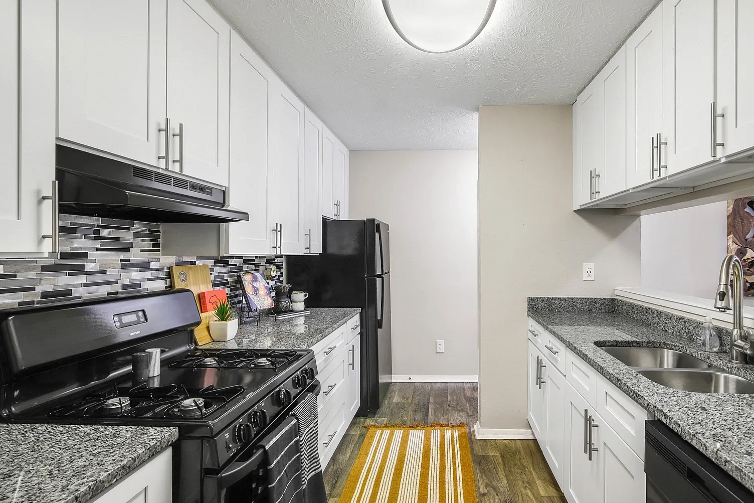 Kitchen with white cabinets, marble style countertops and hardwood style flooring.