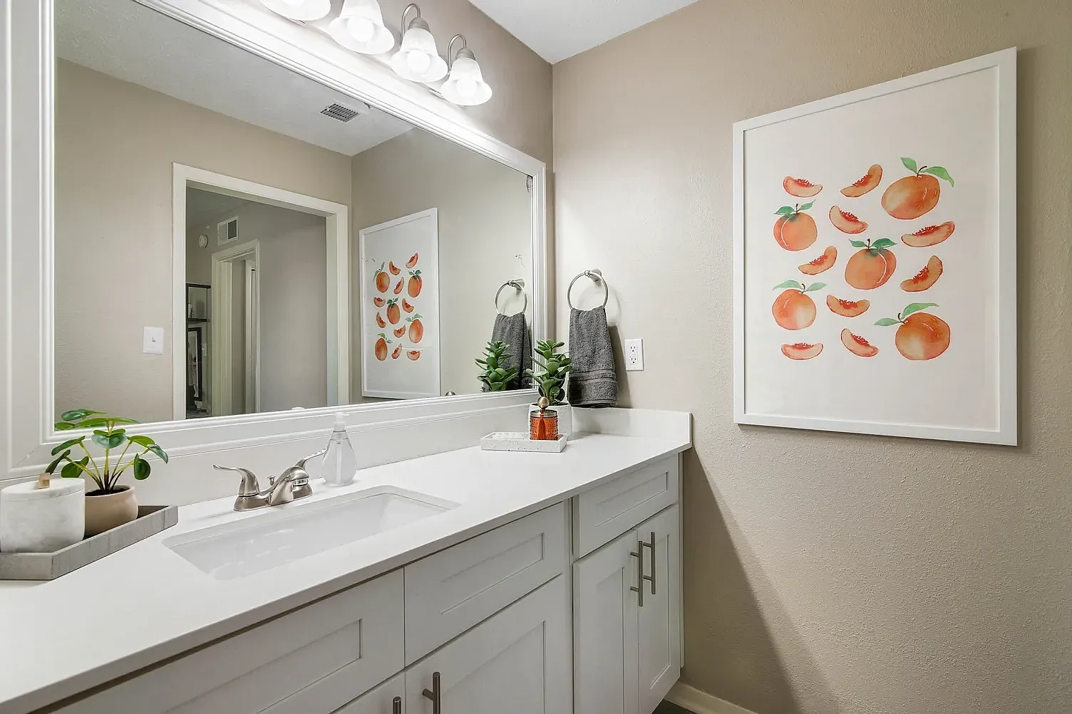 Model bath room with white counters, white cabinets, large mirror and decor