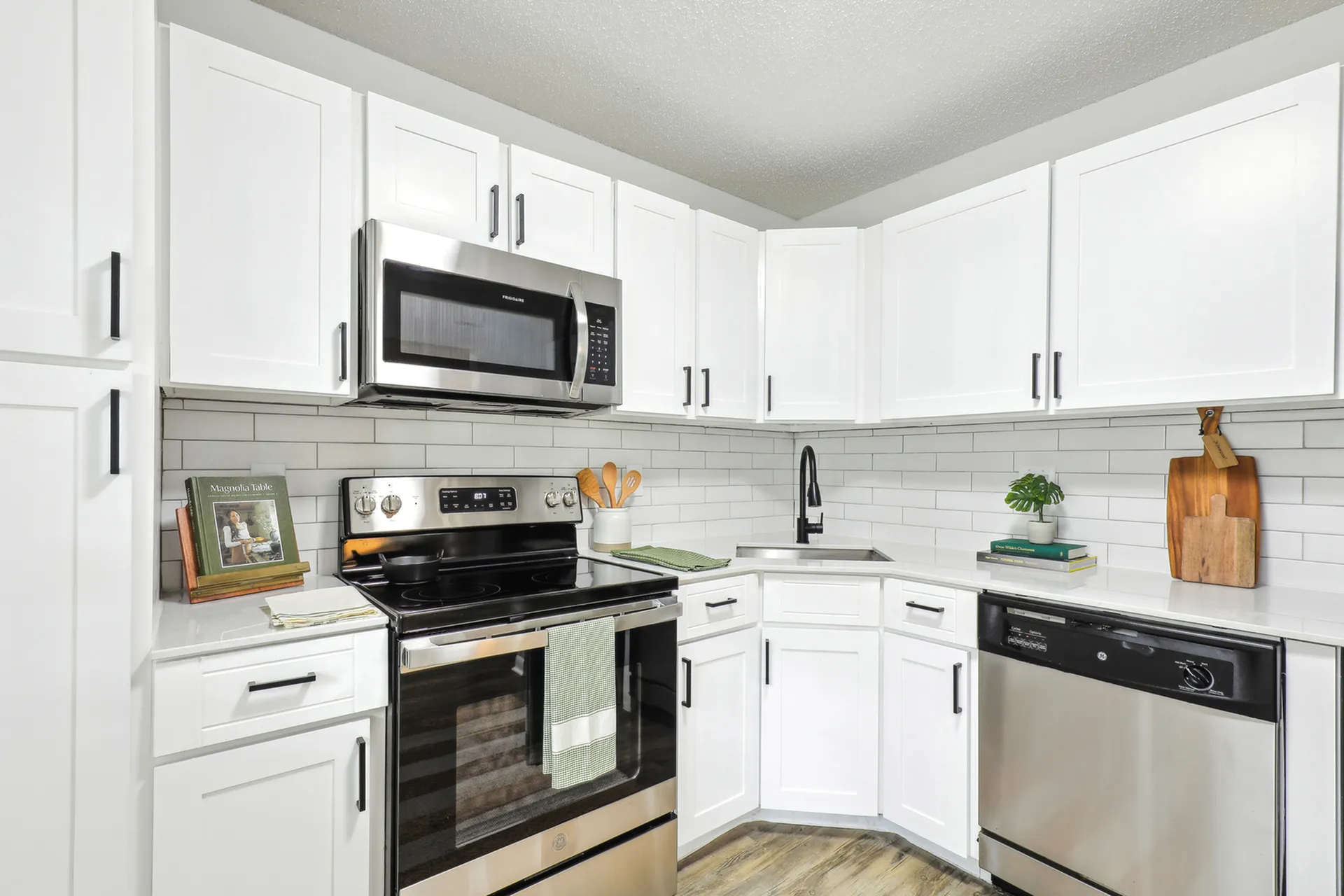 Staged renovated kitchen with white shaker cabinets, white quartz counter tops, white subway backsplash, stainless steel appliances, and hardwood-style flooring.