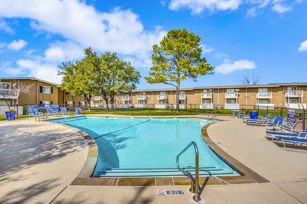 Inviting outdoor pool area with lounge chairs framed by lush trees and modern apartment buildings.
