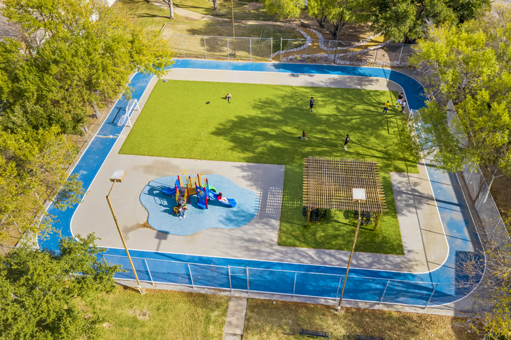 Aerial view of a colorful playground with a lush green field and surrounding blue track.