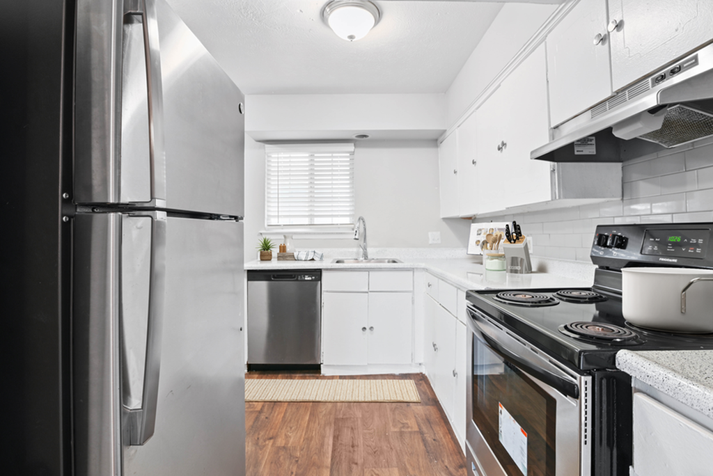 Contemporary kitchen with stainless steel appliances, white cabinetry, and wooden flooring.