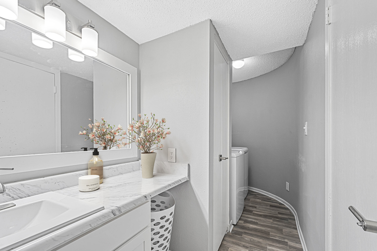 Elegant bathroom with marble countertop, large mirror, and soft lighting, complemented by a modern washing machine nook.