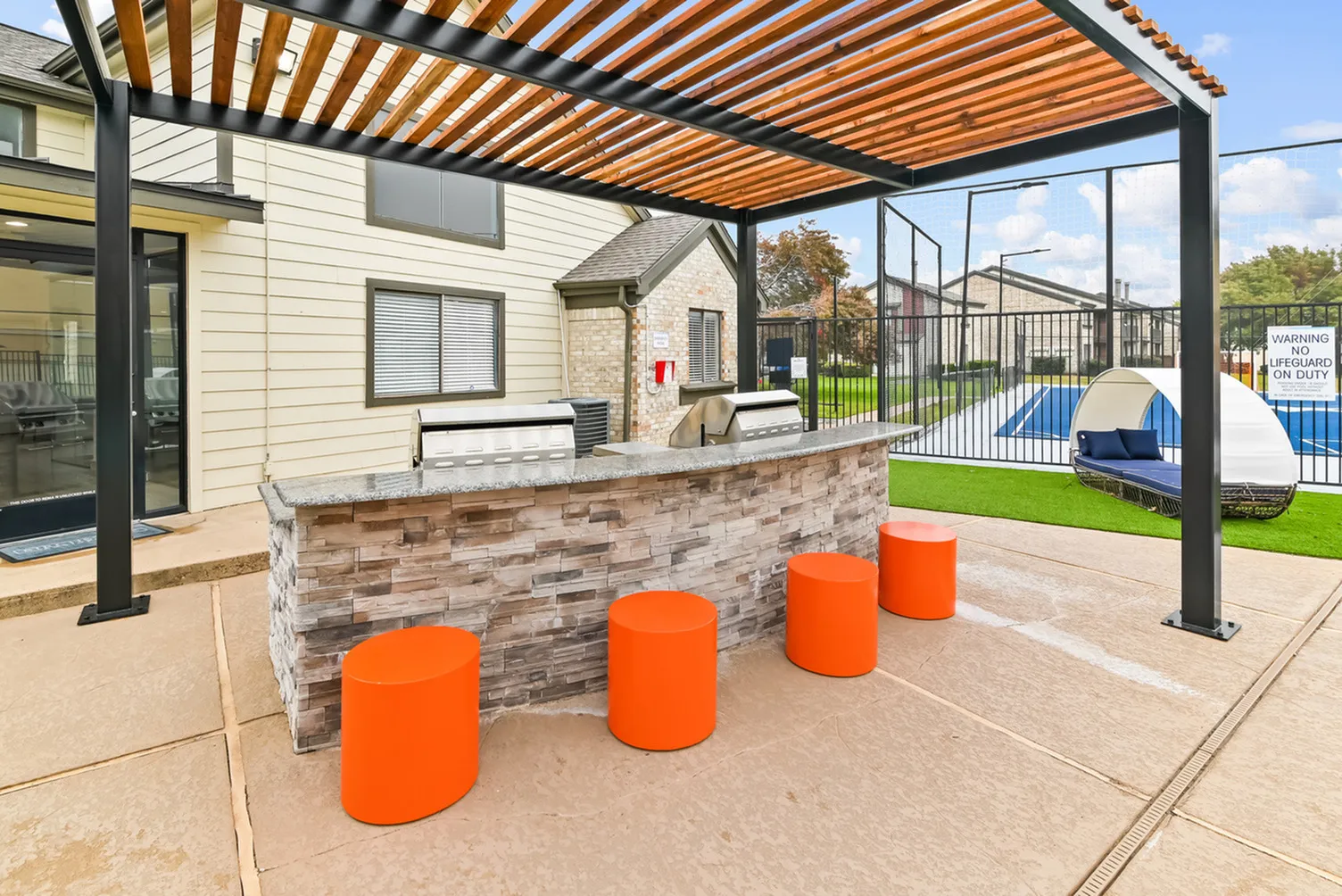 Chic outdoor patio with vibrant orange seating, stone bar, and stylish pergola beside a modern poolside lounging area.
