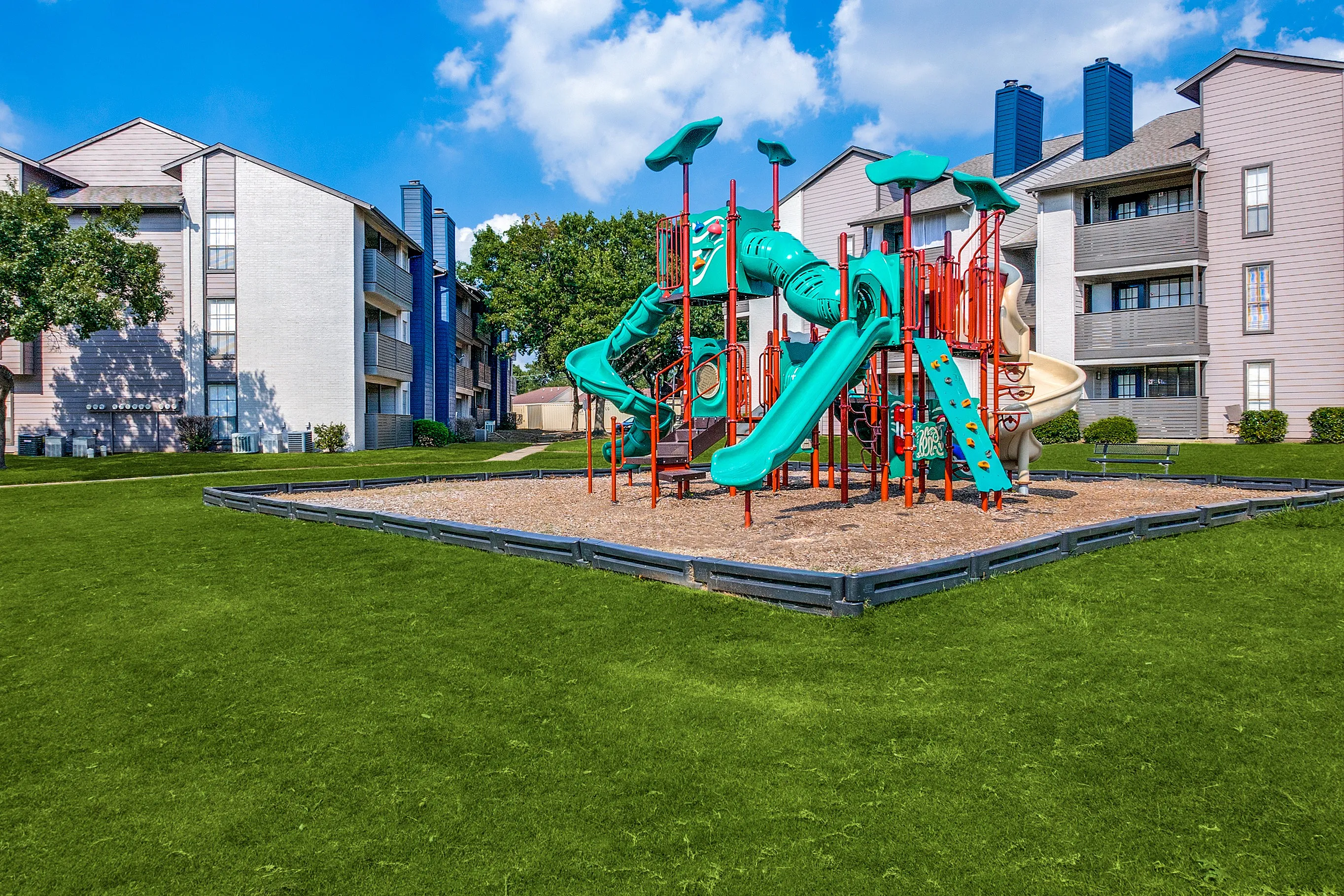 Charming apartment complex with vibrant playground, lush green lawn, and modern architecture for family-friendly living.