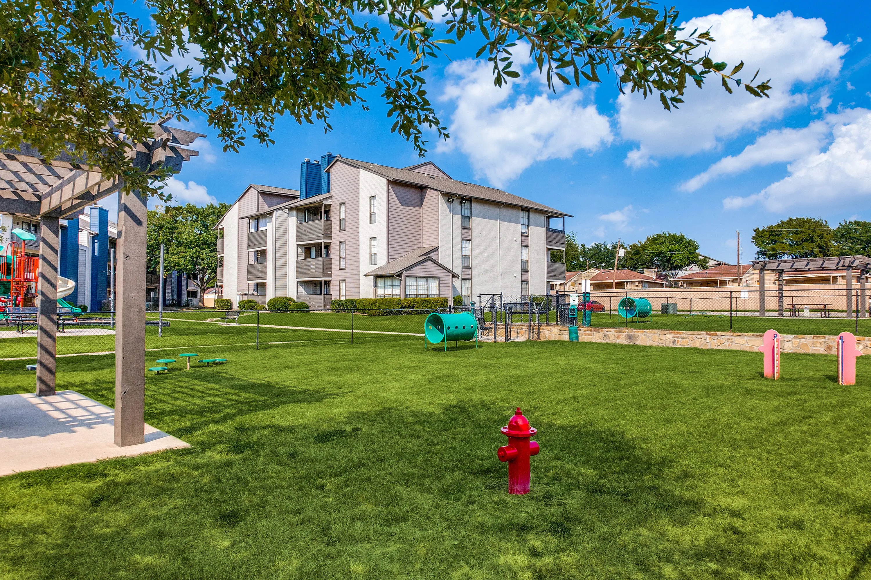 Inviting apartment complex with lush green lawns, vibrant playground, and modern architecture under a bright blue sky.
