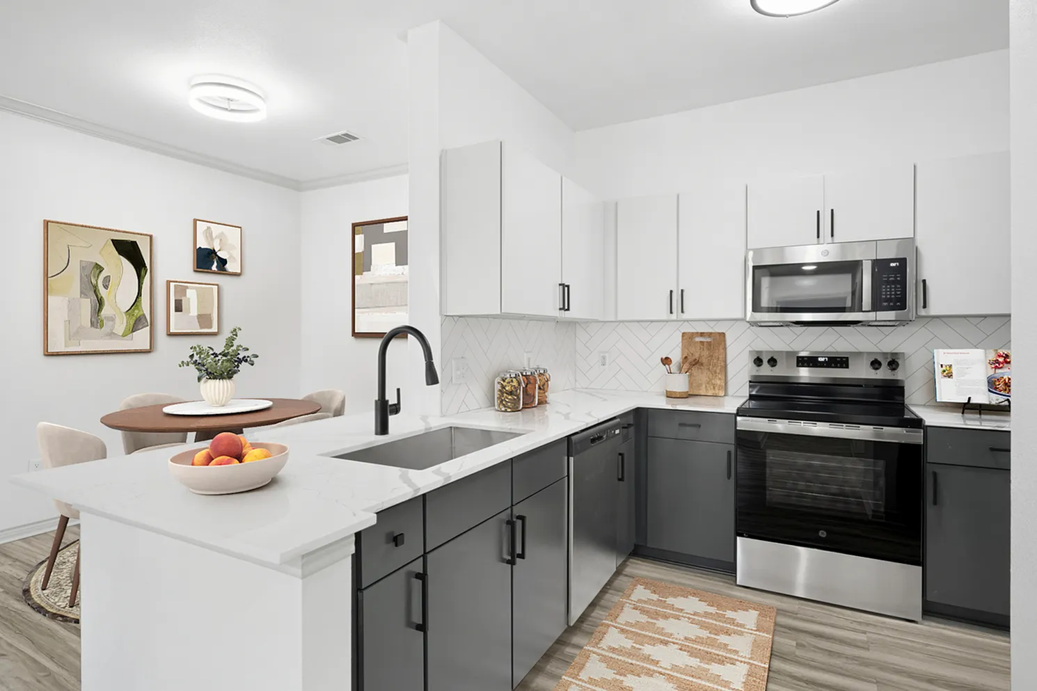 Modern kitchen with sleek black and white cabinetry, stainless steel appliances, and stylish geometric backsplash, adjacent to a cozy dining area with chic art.