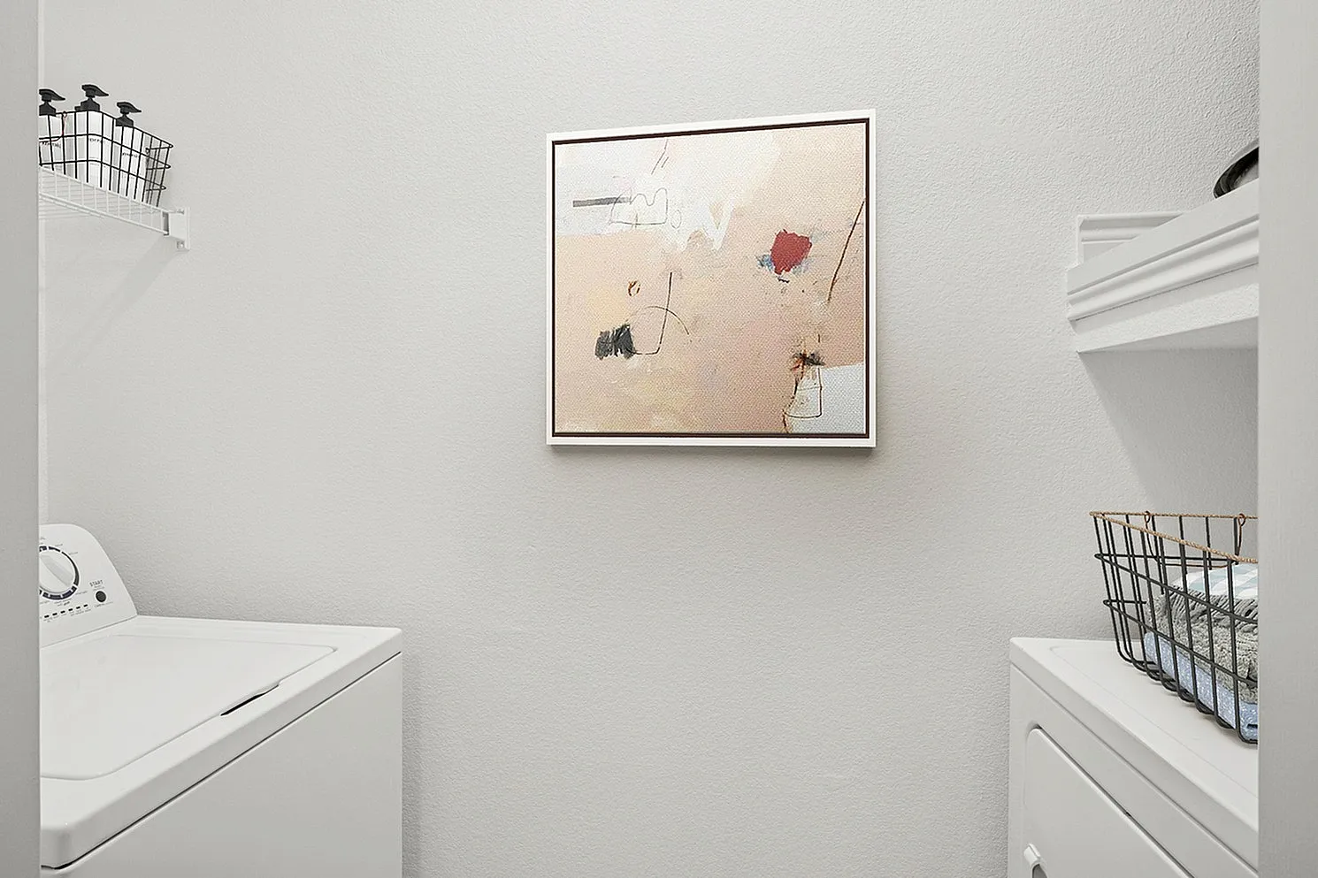 Modern laundry room featuring sleek washer and dryer with elegant abstract art and organized shelving.