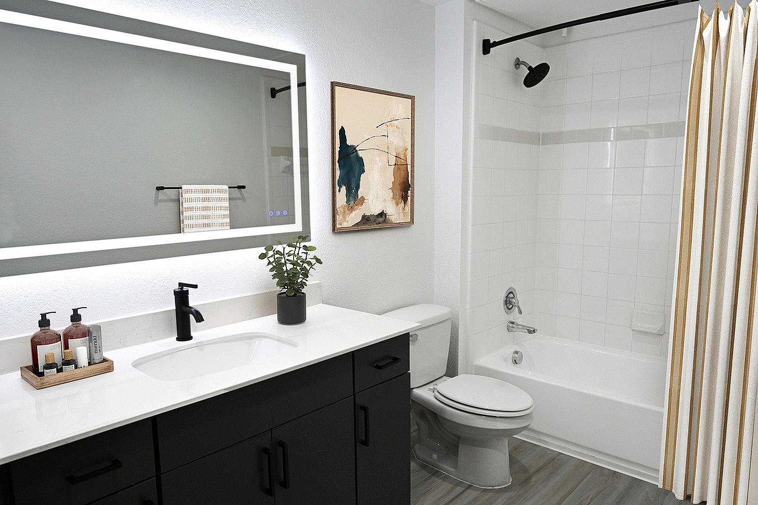 Elegant bathroom featuring a sleek white countertop, modern fixtures, and a large illuminated mirror, with stylish decor and a comfortable bathing area.