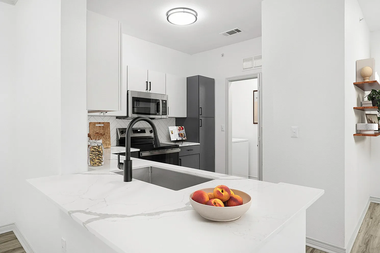 Contemporary kitchen with sleek black fixtures, elegant white cabinetry, and modern appliances, accented by a marble countertop and open shelving.