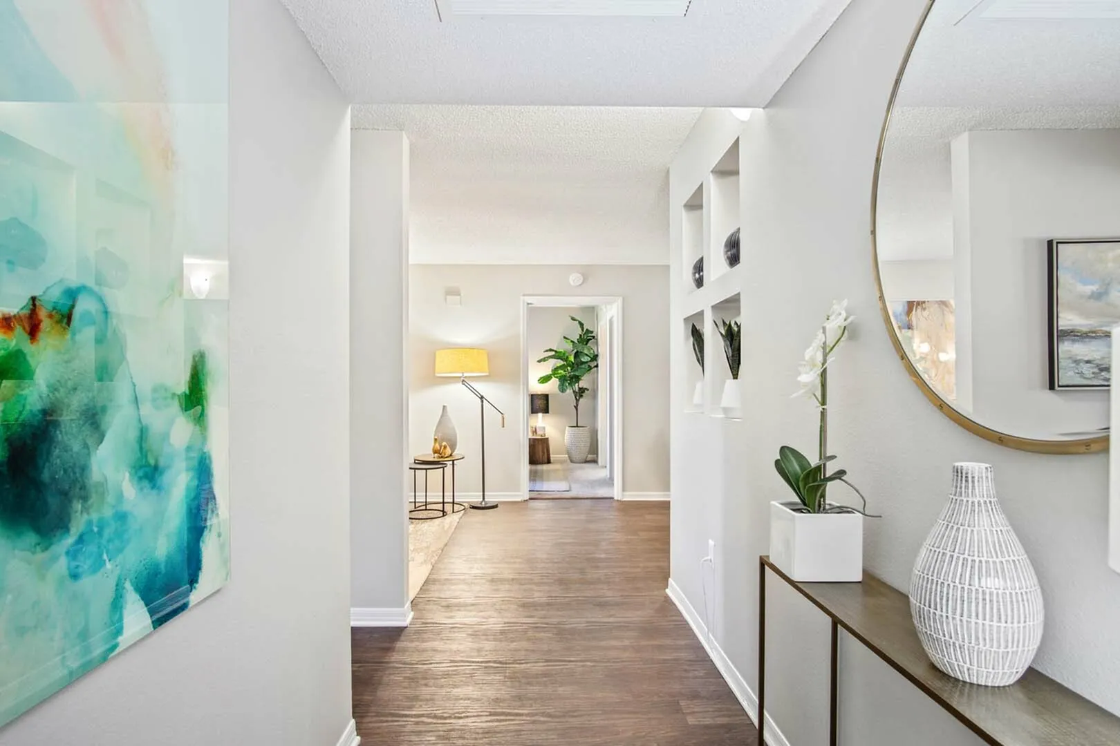 Inviting apartment hallway with modern decor, featuring a stylish console table, contemporary artwork, and a vibrant plant accentuating the bright, open living space.
