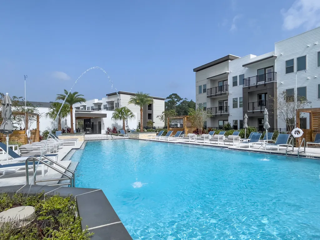 Luxurious apartment complex featuring a sparkling swimming pool surrounded by palm trees and modern architecture, perfect for relaxation and leisure.