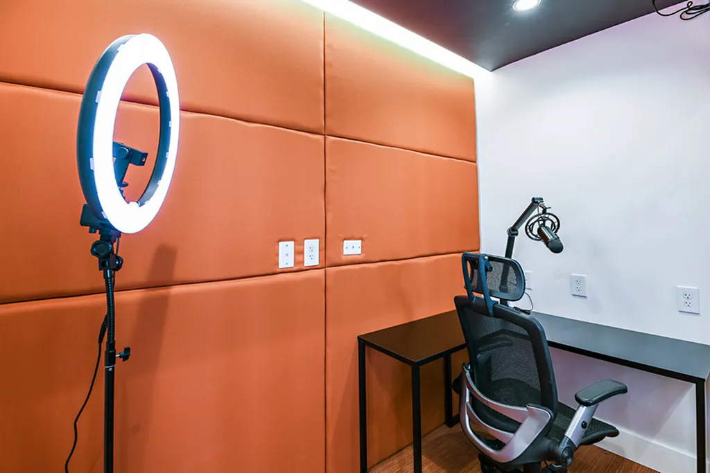 Modern recording studio with vibrant orange acoustic panels, professional microphone setup, ergonomic chair, and sleek lighting.