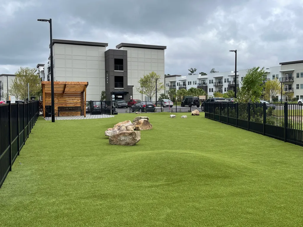 Contemporary apartment complex featuring a spacious dog park with lush green turf, natural rock accents, and a cozy wooden gazebo.