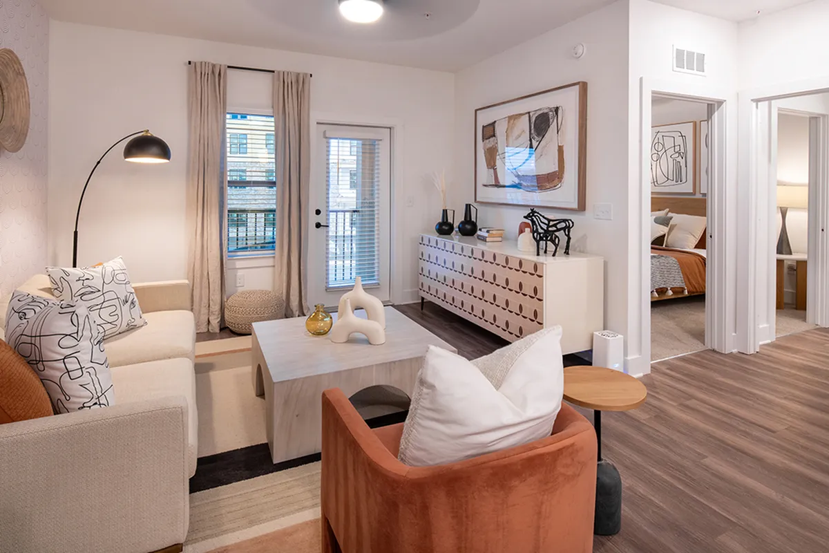Modern living room with stylish decor, featuring cozy seating, artistic elements, and a view into a welcoming bedroom.