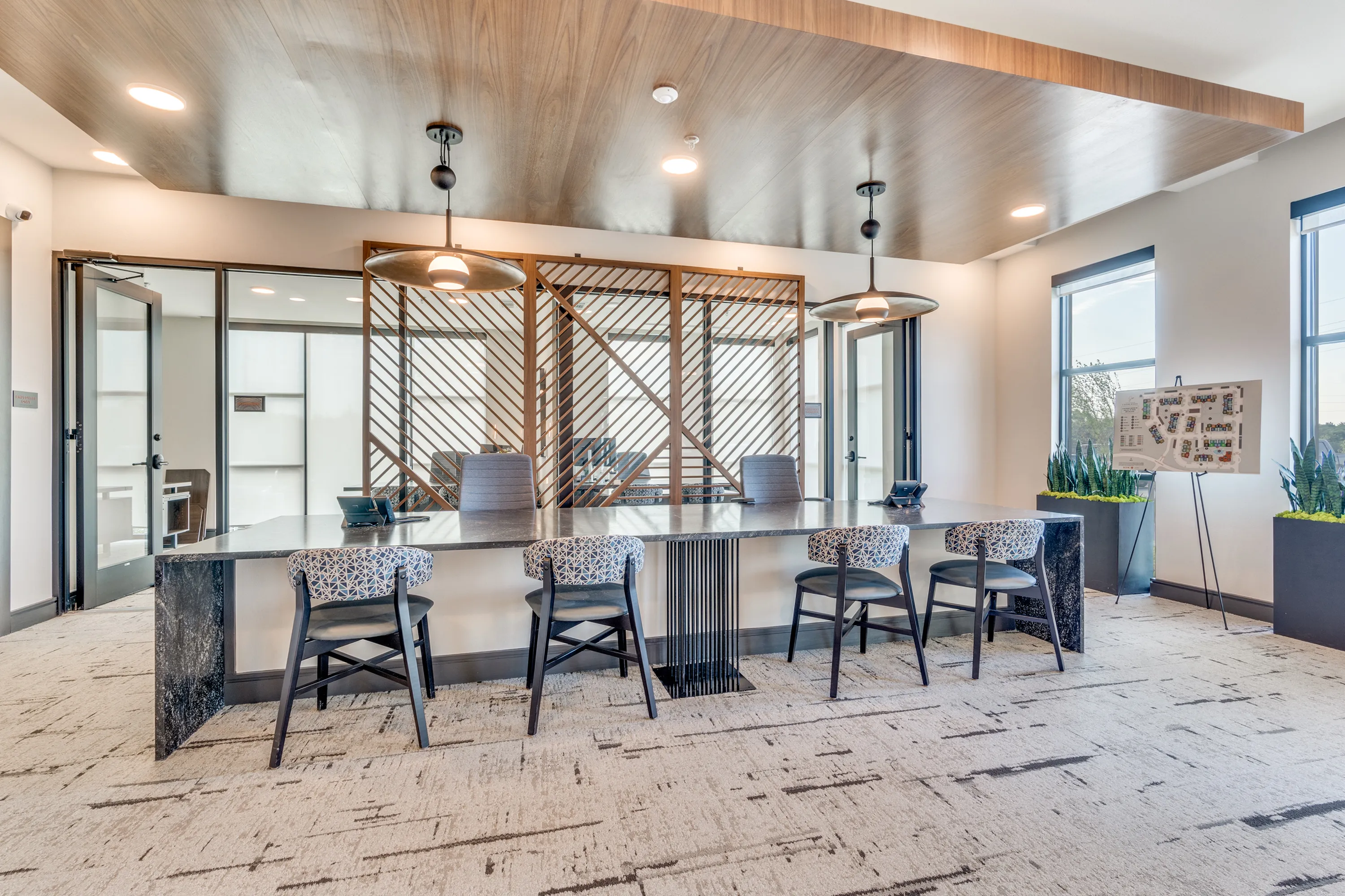 Elegant conference room with stylish chairs, modern lighting, and a polished granite table, accentuated by natural light and greenery for a professional ambiance.