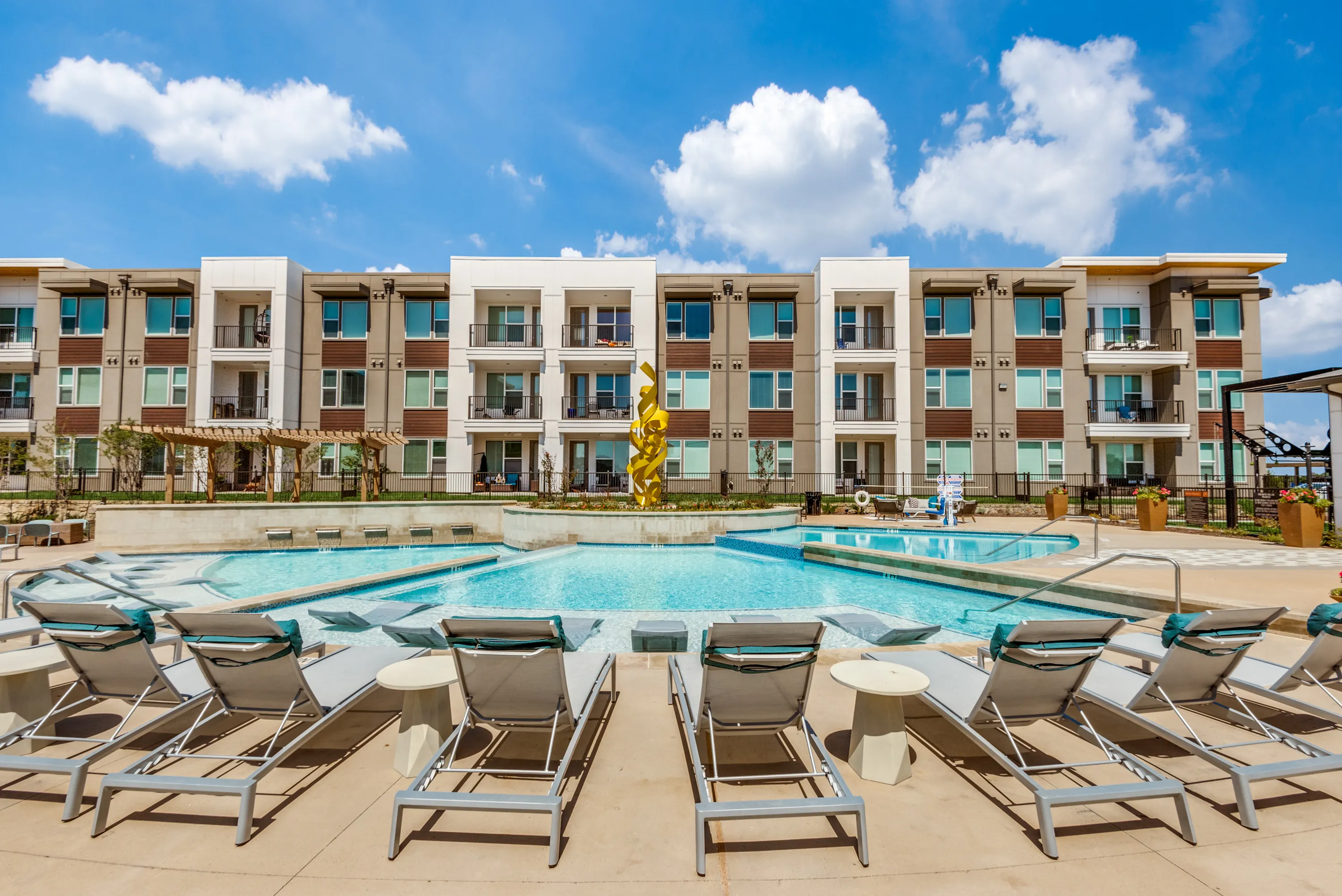 Luxurious apartment complex featuring a sparkling pool with stylish sun loungers, modern architecture, and vibrant outdoor ambiance.