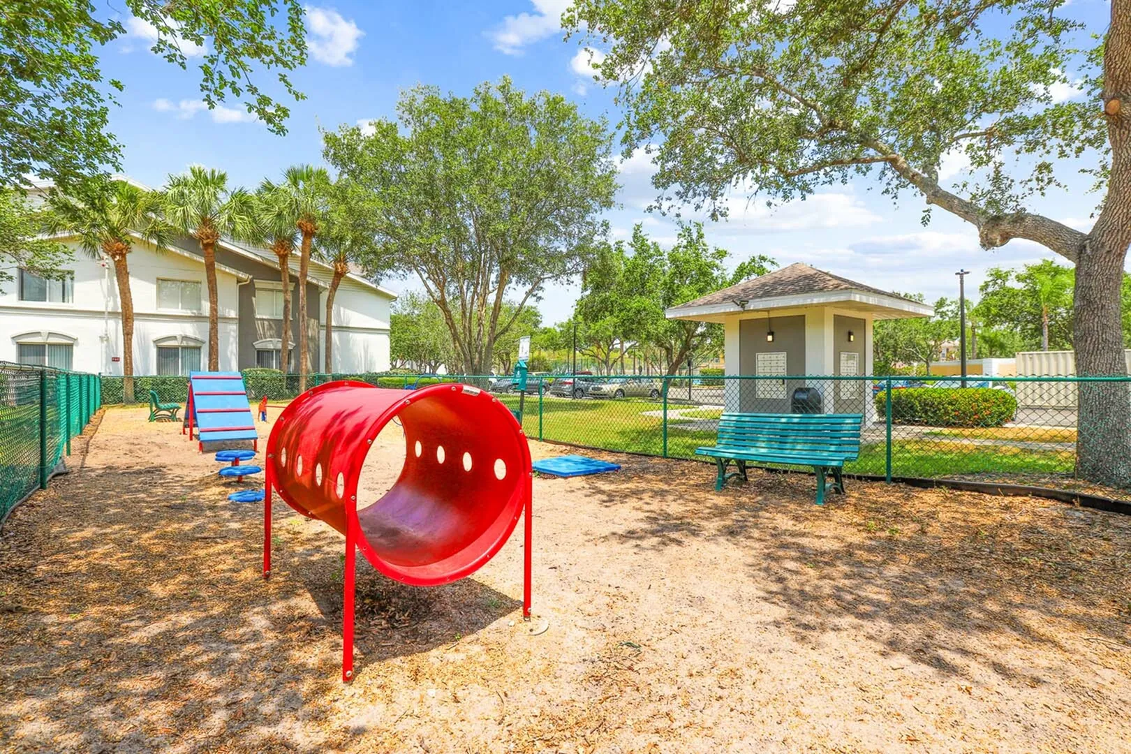 Vibrant pet-friendly playground with agility equipment, surrounded by lush greenery and shaded seating, perfect for outdoor enjoyment.