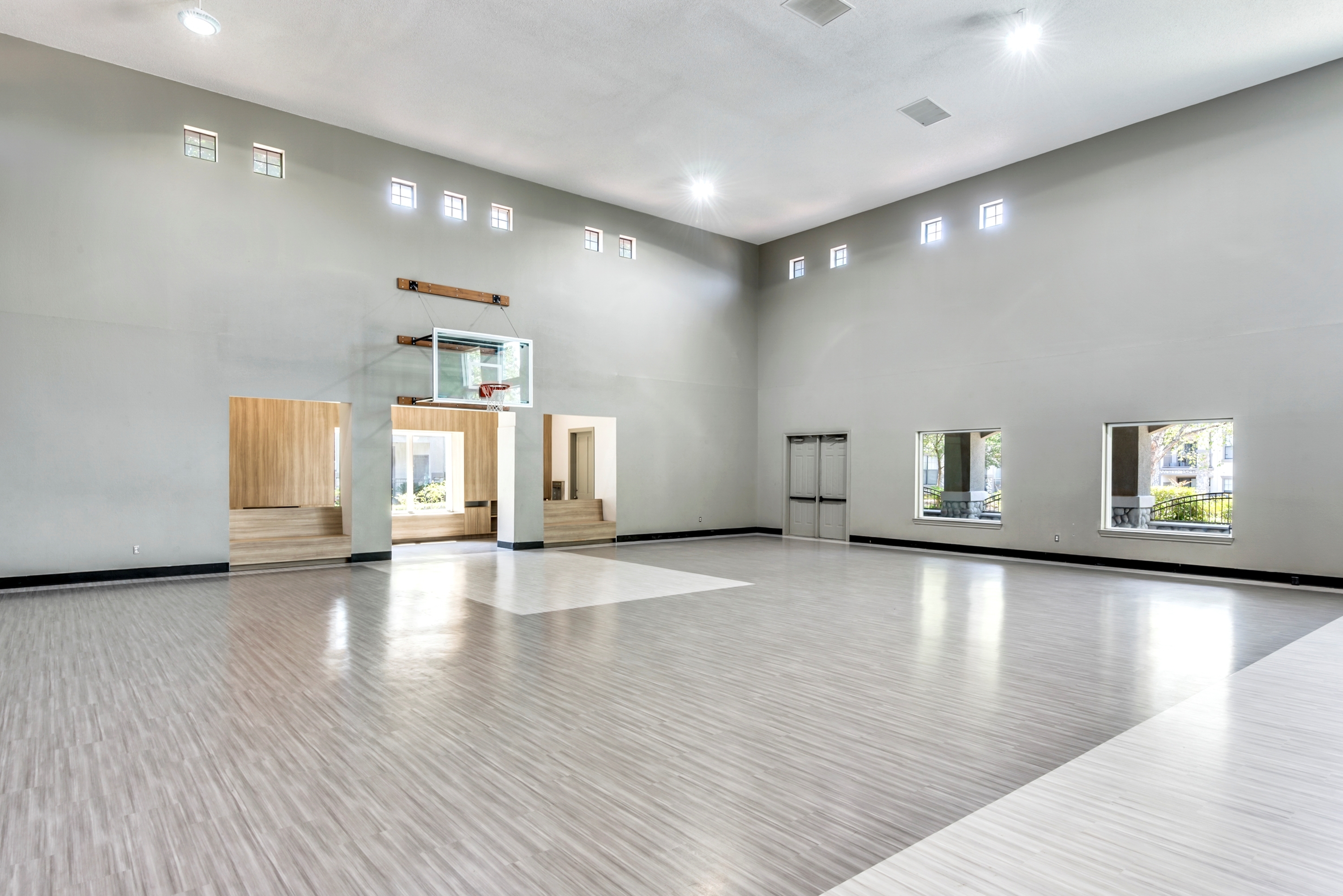 Expansive indoor basketball court with sleek flooring, high ceiling, and ample natural light from large windows.