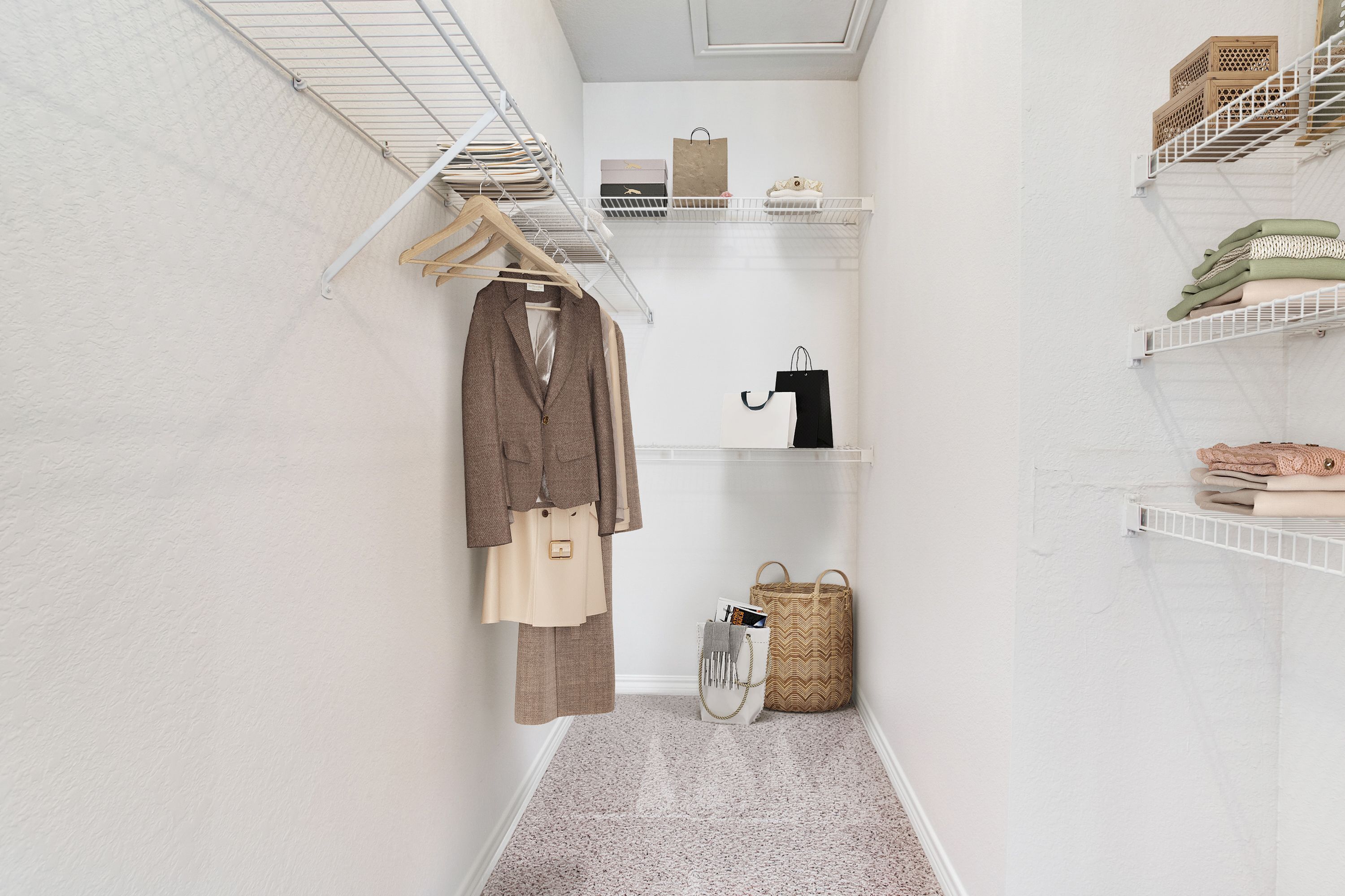 Spacious and elegantly organized walk-in closet with stylish clothing and accessories, featuring white shelving and a plush carpet floor.