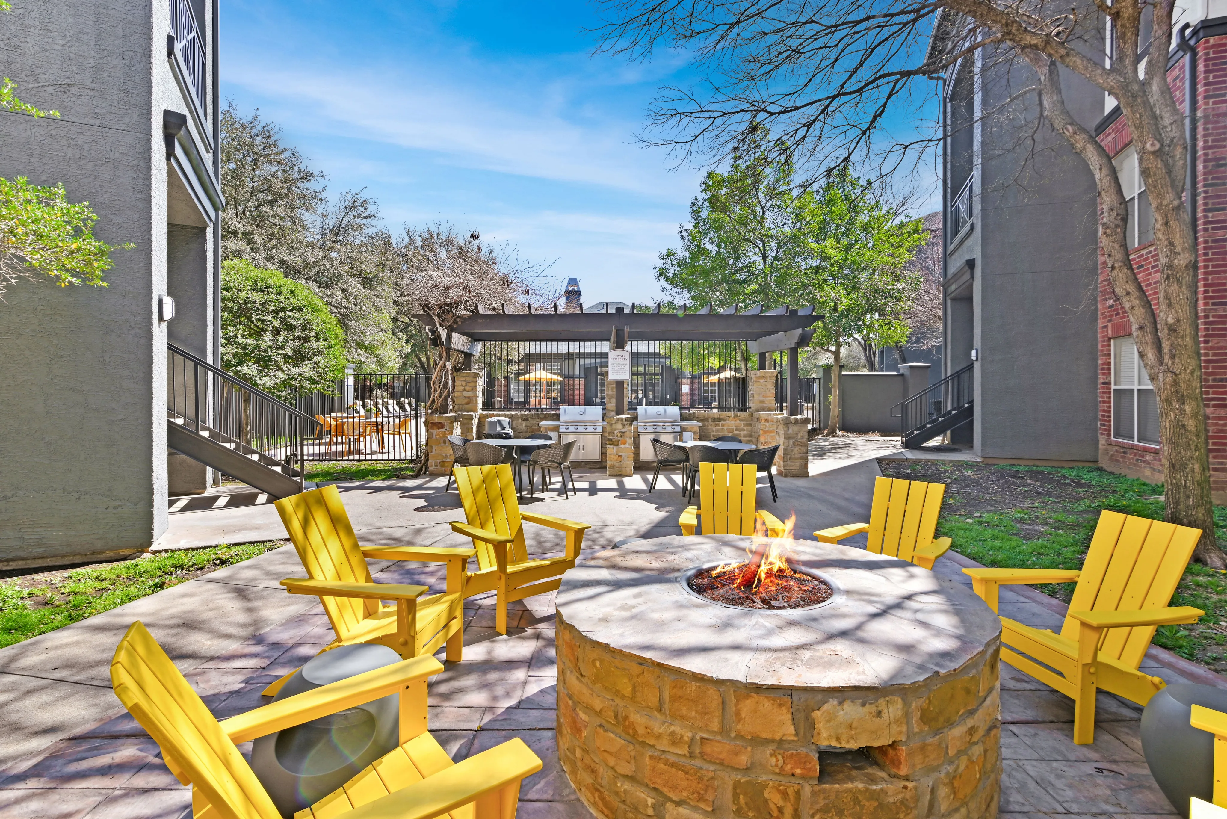 Inviting outdoor area with vibrant yellow chairs surrounding a cozy fire pit, adjacent to a stylish BBQ grill station under a pergola.