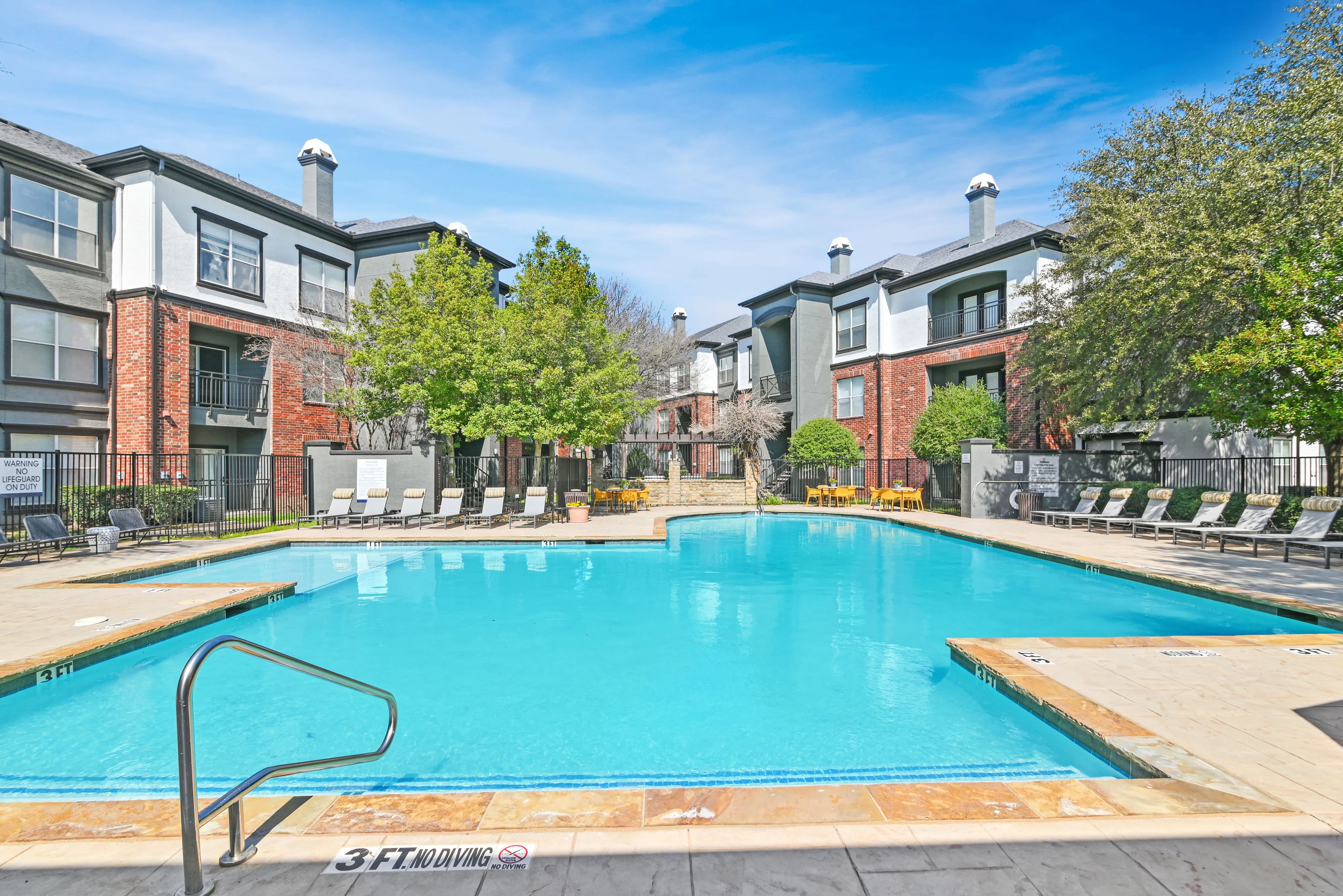 Inviting apartment community with a sparkling swimming pool surrounded by lounge chairs and lush greenery, offering a serene and luxurious outdoor experience.