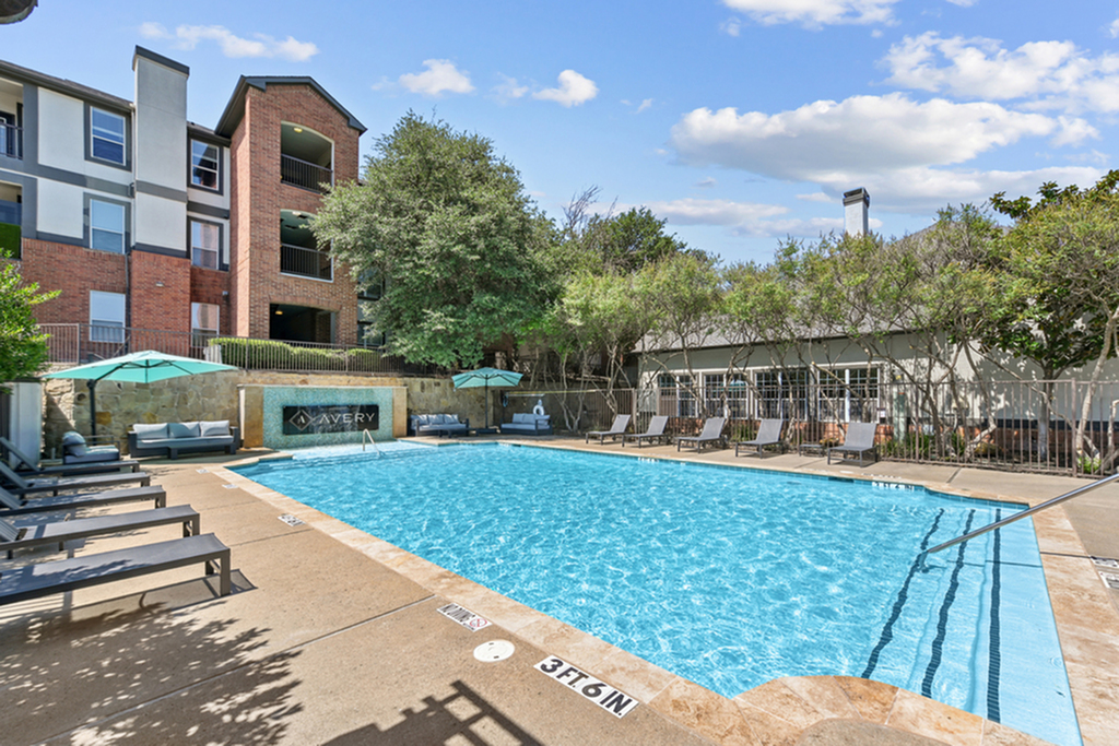 Swimming pool area with chic lounge chairs and umbrellas, set against a backdrop of modern apartment buildings and lush greenery.