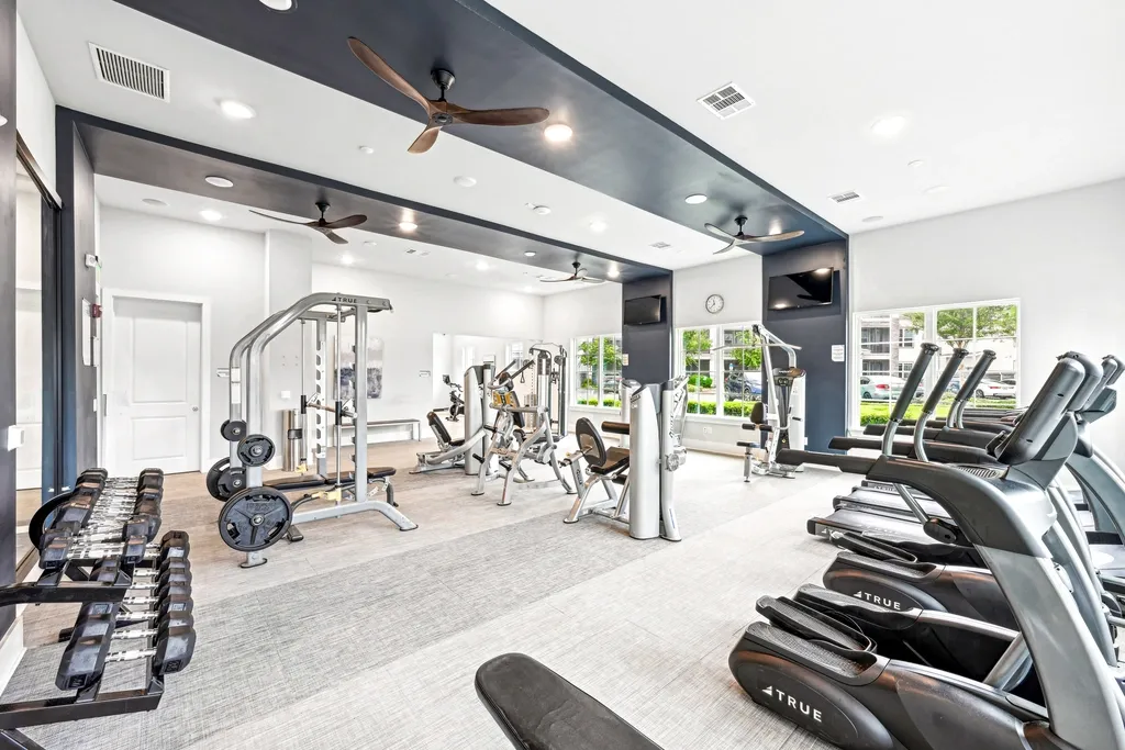 Large, modern fitness center with a variety of cardio and strength equipment, free weights, and spacious layout with high ceilings and natural light.