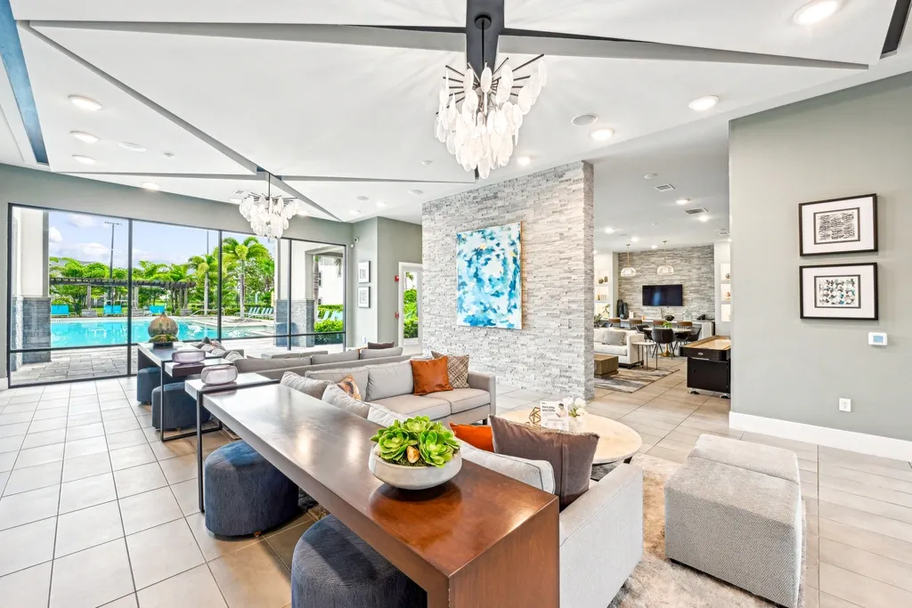 Modern clubhouse lounge with stylish seating, decorative lighting, and an open layout, featuring large windows with views of the pool and adjacent gathering spaces.