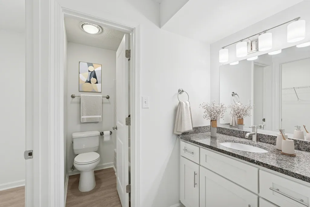 Modern bathroom with elegant granite countertop, stylish vanity lighting, white cabinetry, and contemporary decor.