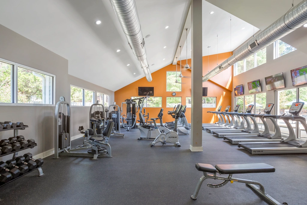 Bright and modern fitness center with state-of-the-art exercise equipment, featuring treadmills, weight benches, and strength training machines, illuminated by natural light through large windows.