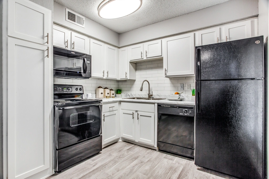 Modern kitchen with white cabinets, marble-style countertops, and black appliances, including an electric stove, microwave, dishwasher, and refrigerator. Features a subway tile backsplash, hardwood-style flooring, and simple countertop decor for a clean, updated look.