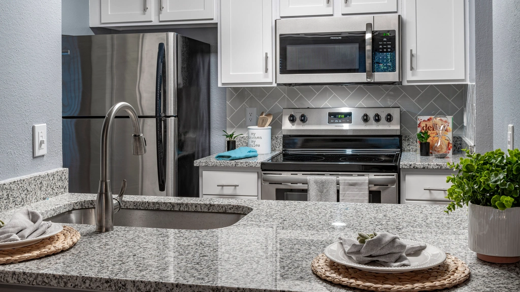 Modern kitchen with white cabinets, stainless steel appliances, and a gray herringbone backsplash, featuring a granite countertop with an undermount sink and decorative place settings.