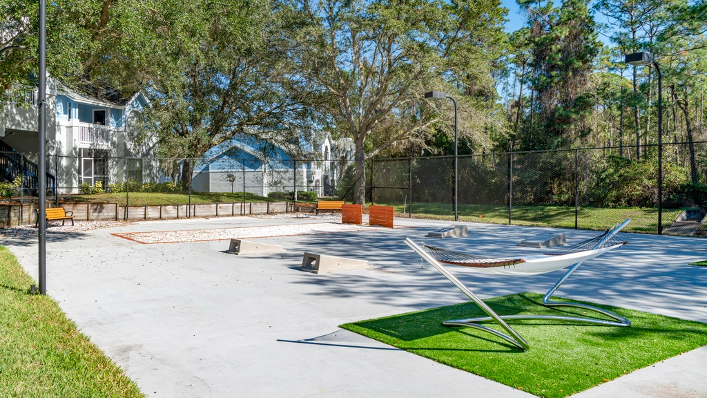 Outdoor recreational area with seating, hammock lounge, corn hole, horseshoes and open space, surrounded by trees and residential buildings.