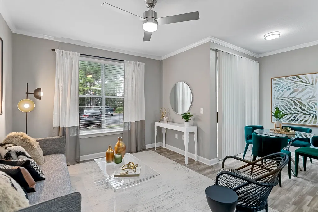 Bright modern apartment living and dining area featuring hardwood-style flooring, crown molding, large windows with natural light, contemporary furnishings, a ceiling fan, and a stylish dining space with velvet accent chairs.