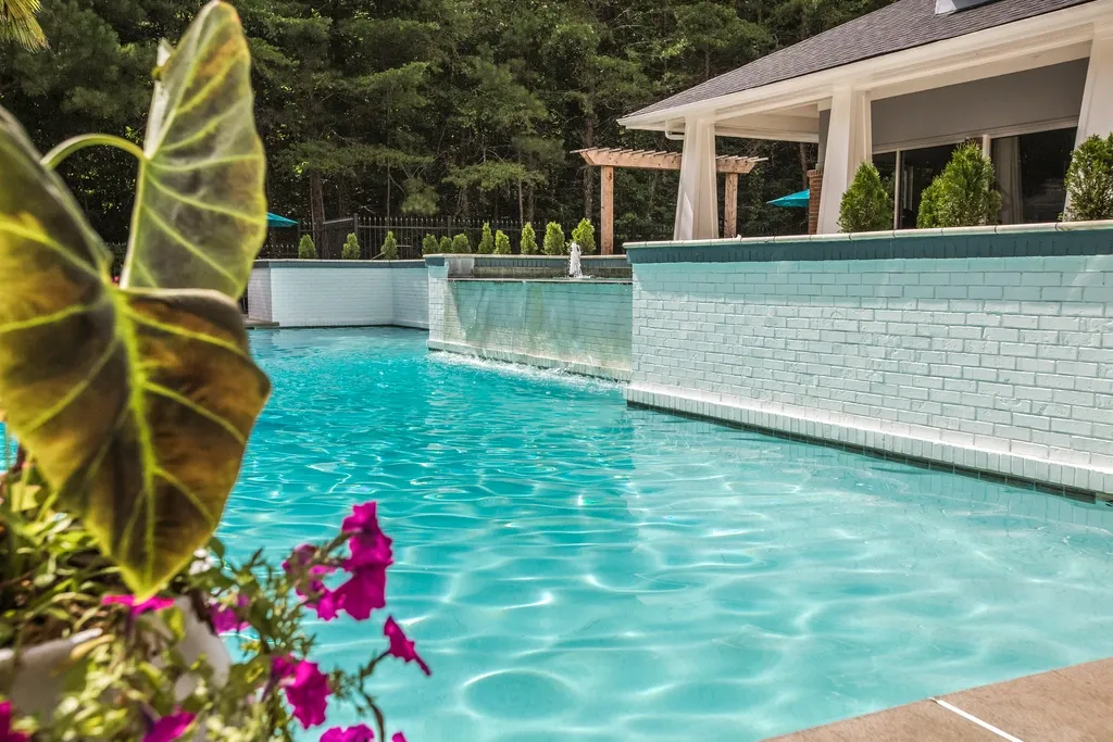Resort-style apartment swimming pool with crystal-clear water, elegant water features, lush landscaping, and a relaxing outdoor lounge area surrounded by mature trees.