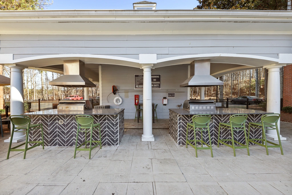 Covered outdoor grilling pavilion with stainless steel grills, bar-style seating, tiled countertops, and a spacious entertaining area located beside the resort-style pool.