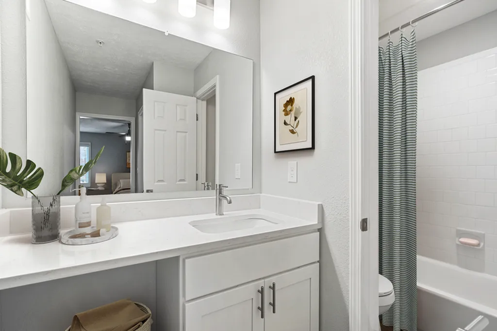 Bright and modern bathroom featuring a large vanity with sleek fixtures, a decorative framed art piece, and an inviting shower area.