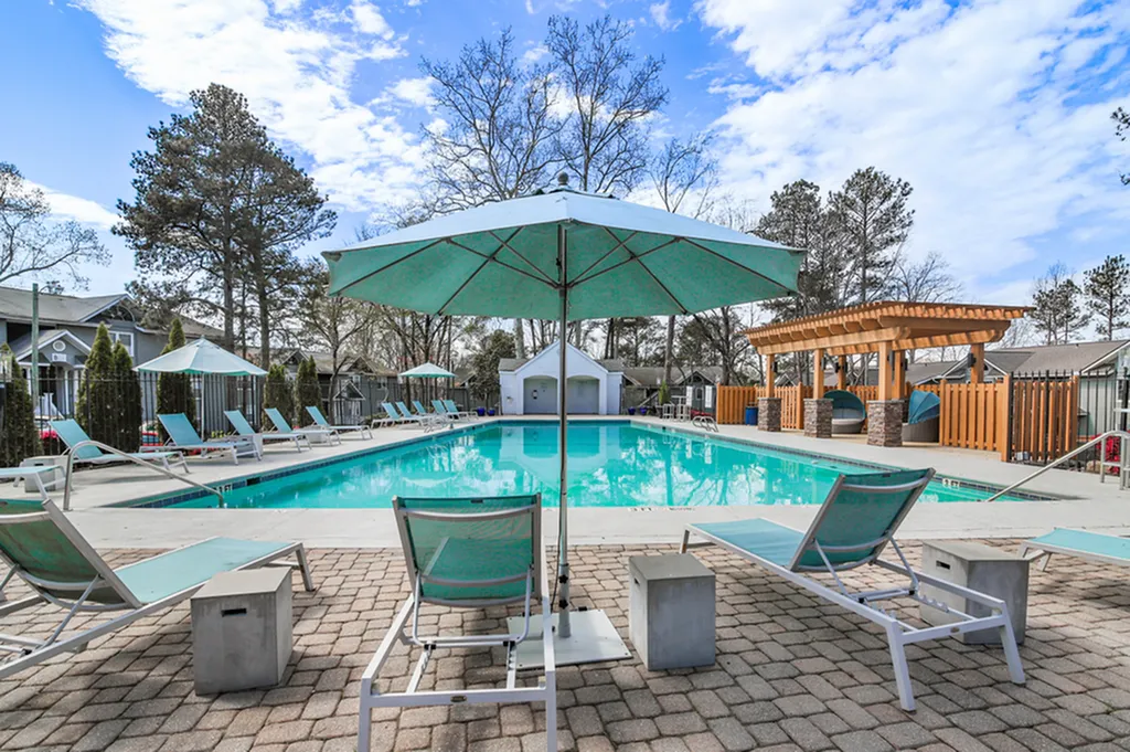 Inviting outdoor pool area with modern lounge chairs and umbrellas, surrounded by lush greenery and a stylish pergola.