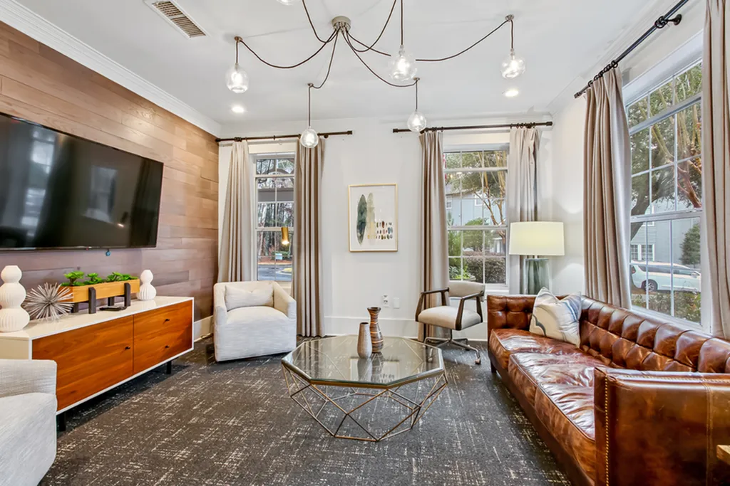 Inviting modern clubhouse featuring elegant decor, plush leather sofa, sleek armchairs, large flat-screen TV, and abundant natural light from expansive windows.