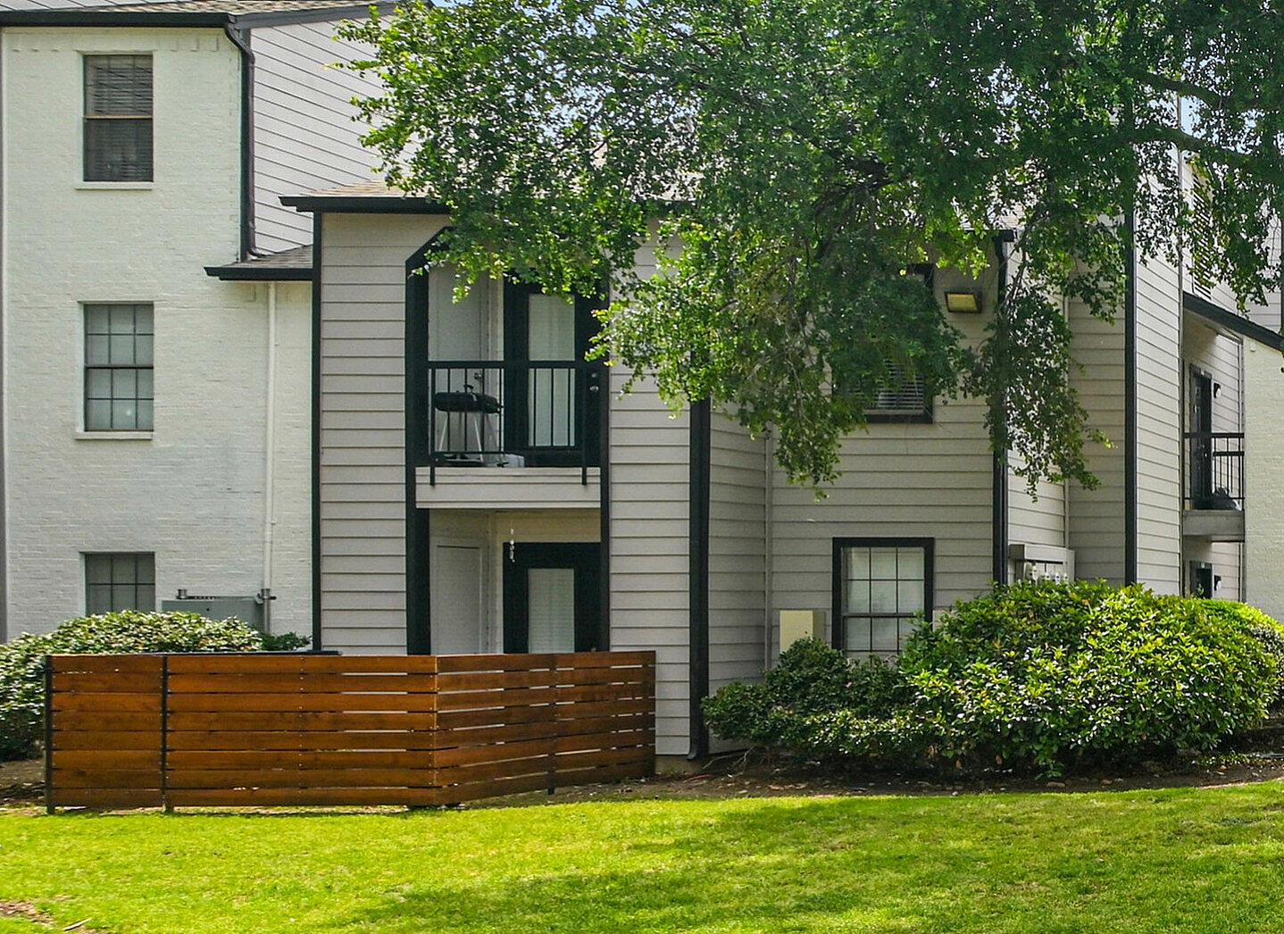 Charming apartment complex with lush green lawns, mature trees, and modern three-story buildings, offering a serene and inviting environment.