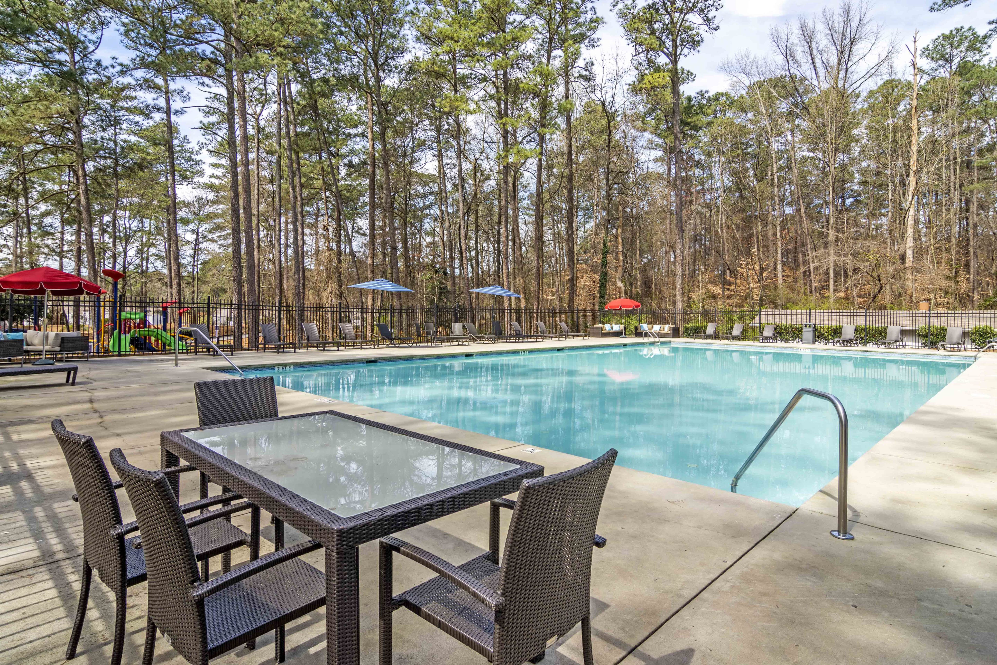 Inviting outdoor pool area surrounded by lush greenery, featuring comfortable lounge chairs and shaded tables for leisurely relaxation.