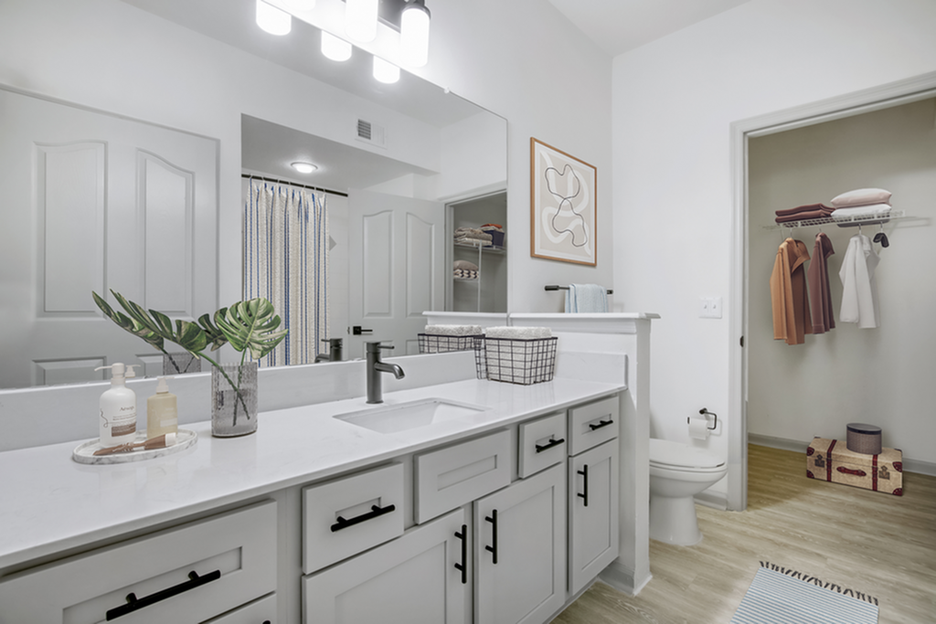 Elegant bathroom with sleek white countertops, modern fixtures, and an open walk-in closet, exuding a spa-like ambiance.