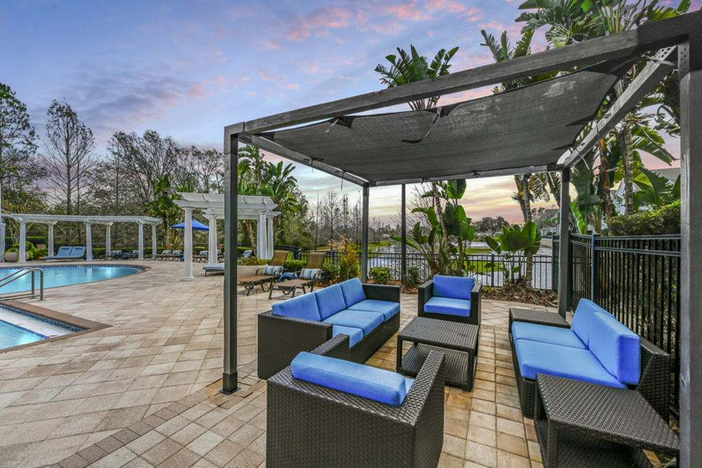 Luxurious outdoor pool area with stylish blue seating under a pergola, surrounded by lush greenery and a stunning sunset view.